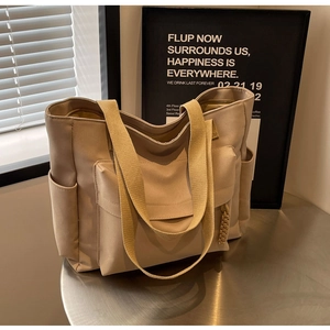 Detail of a large khaki canvas tote bag featuring functional front and side pockets on a table