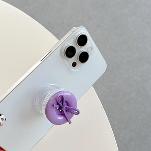 Close-up of a purple button phone grip with a suede bow on a white smartphone