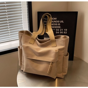Detail of beige canvas tote bag showing multi-pocket structure and woven zipper puller