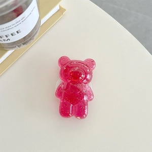 Detail shot of a clear pink bear phone grip with gold foil flakes on a desk
