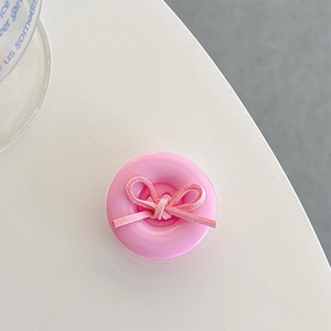 Detailed view of a pink button phone grip with a soft velvet bow on a white desk
