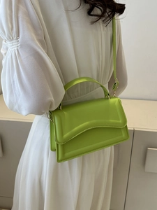 Detail of lime green leather handbag with streamline flap design worn by model