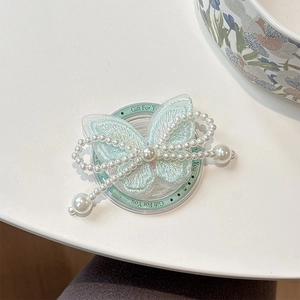 Macro detail of mint green embroidered butterfly phone grip with white pearl tassels