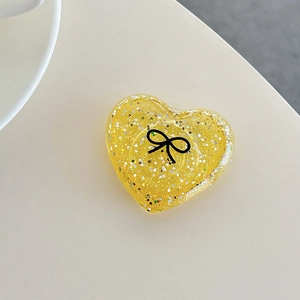 Macro view of a yellow resin heart phone grip with glitter and a black bow design