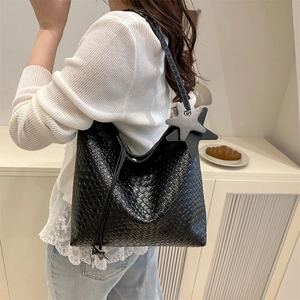 Black woven leather tote bag with star pendant on a female model in minimalist setting