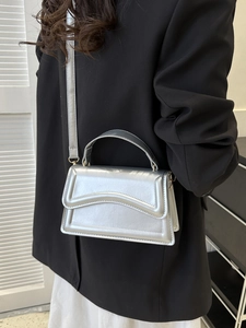 Detail of silver metallic handbag featuring wavy embossed flap and adjustable shoulder strap