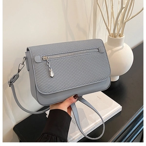 Detail of grey crossbody bag featuring woven texture flap and front zipper with silver charm