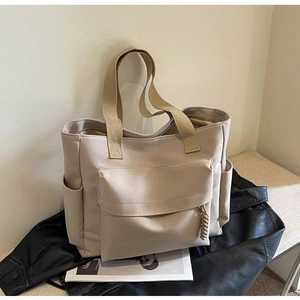 Detail view of large beige canvas tote bag with front flap pocket and wide fabric strap