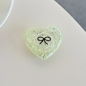 Macro view of heart-shaped glitter phone grip with black bow pattern in mint green resin
