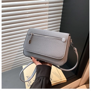 Detail of grey-blue crossbody bag featuring woven texture flap and metallic zipper