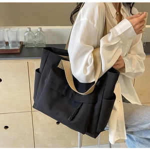 Detail of a large black canvas tote bag with khaki straps and front pocket for commute