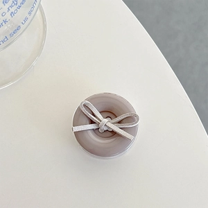 Detail of a grey button-shaped phone grip featuring a soft grey fabric bow accent