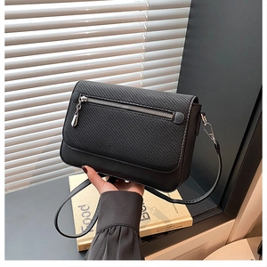 Detail of black crossbody bag featuring textured fabric flap and sleek leather base