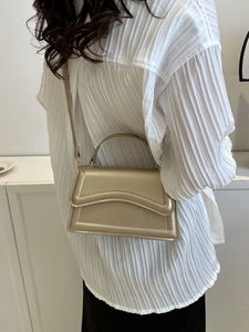 Champagne gold faux leather handbag with wave flap and metallic finish on model