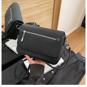 Detail of black crossbody bag with textured flap and silver metal zipper on mirror