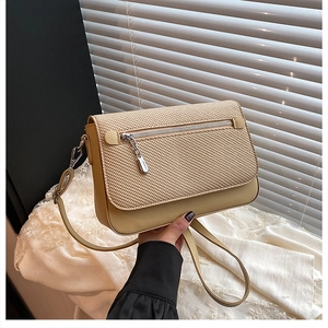 Detail showing the beige woven texture flap and silver zipper charm on the shoulder bag