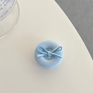 Detail view of light blue button phone grip with a suede bow on a clean white desk