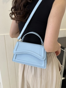 Close-up of light blue leather handbag with flap design worn by a model in a minimal setting