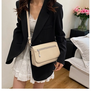 Beige woven texture crossbody bag shown on model wearing black blazer and white skirt