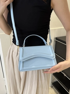 Detail of light blue crossbody bag featuring a unique wavy flap and adjustable strap