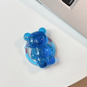 Detail view of a blue translucent bear phone stand with gold flakes and Good Luck text