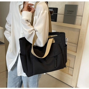 Detail of canvas tote bag with khaki straps and large front pocket shown on shoulder