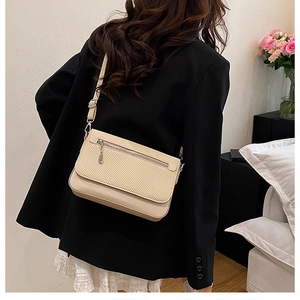 Detail of a beige crossbody bag with woven texture worn by a model in a black blazer