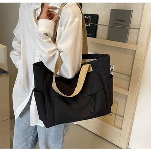 Side view of a black canvas tote bag with khaki straps worn by a model in a library