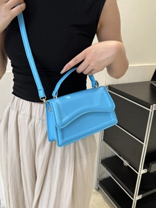 Detail of light blue crossbody bag featuring a curved flap and adjustable shoulder strap