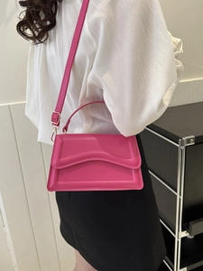 Side view of a rose pink handbag featuring a unique curved flap and adjustable strap