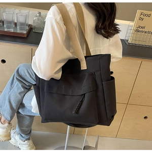 Detail of black canvas tote bag showing front flap pocket with woven knot and side pocket
