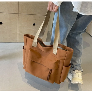 Detail of dark caramel canvas tote bag with beige webbing handle and large front pocket