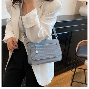 Detail of light blue crossbody bag featuring woven texture and silver zipper accents