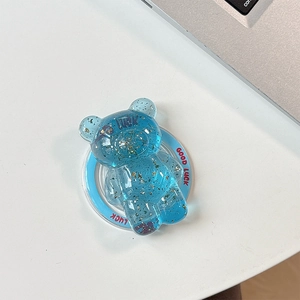 Detail view of a blue transparent bear phone stand with gold foil flakes and Good Luck text