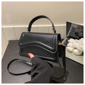 Detail of black faux leather handbag with wavy flap design and gold hardware on wooden desk