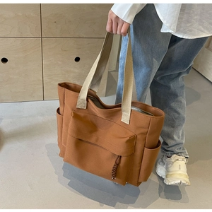 Brown canvas tote bag detail featuring large front pocket and beige strap handles