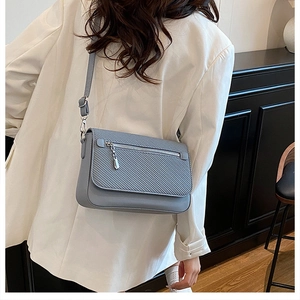 Detail of light blue crossbody bag featuring woven texture flap and metal zipper pocket