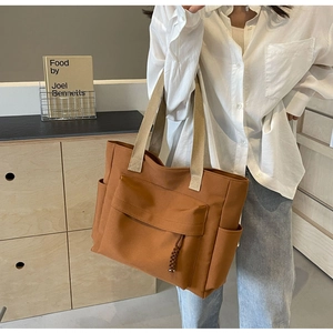 Close-up of brown canvas tote bag featuring wide beige straps and front flap pocket detail