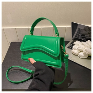 Detail of a bright green crossbody bag with wavy flap design and smooth top handle