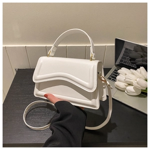Detail of white leather handbag with wave stitching and gold hardware on a desk