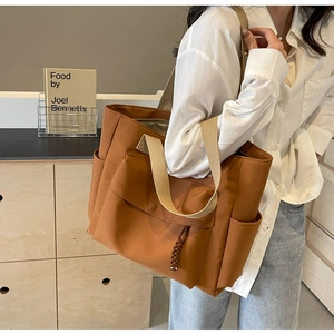 Detail view of large brown canvas tote bag featuring front pocket and rope puller accent