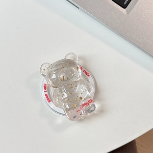 Macro shot of bear-shaped phone stand with gold foil details and Good Luck text on white desk