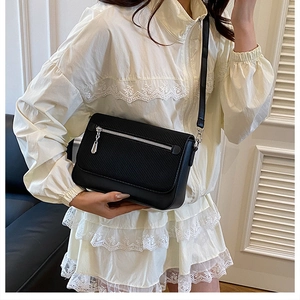 Detail of black crossbody bag featuring dual-textured fabric and silver front zipper