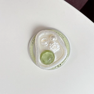 Detail of magnetic phone grip featuring cream pebble base with green gem and pearl accents