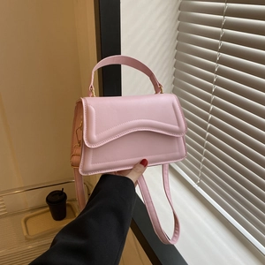 Close-up of light pink crossbody bag with wavy stitching and gold hardware detail