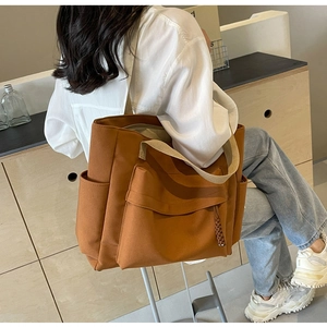 Detail view of large brown canvas tote bag with front pocket and wide strap on model