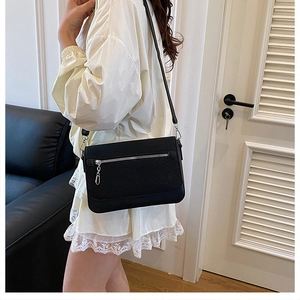 Detail of black textured crossbody bag with silver zipper and slim leather shoulder strap