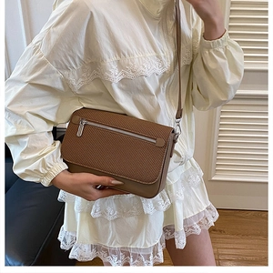 Detail view of a brown woven texture crossbody bag with zipper accent and adjustable strap