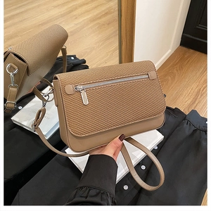 Detail of a brown crossbody bag featuring a textured woven flap and silver metal hardware