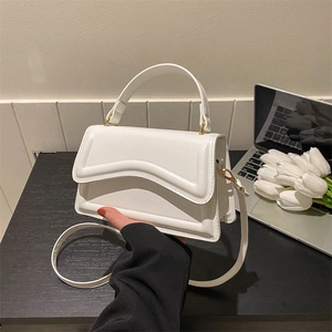 White leather handbag with unique wavy flap and gold hardware on an office desk